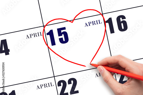 A woman's hand drawing a red heart shape on the calendar date of 15 April. Heart as a symbol of love.