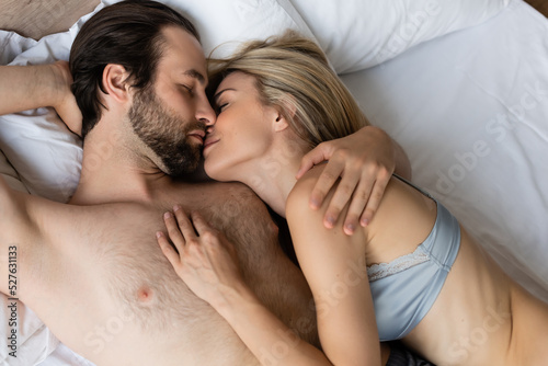 top view of sexy couple hugging and kissing with closed eyes on bed.