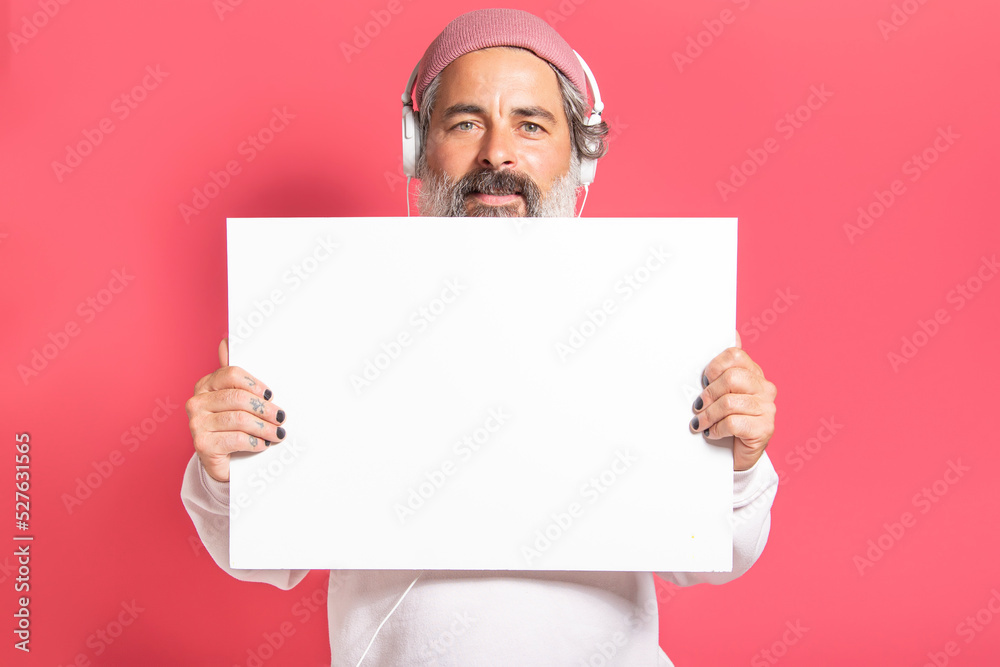 Mature modern man in headphones holding poster over pink wall Mature modern man in headphones holding poster over pink wall