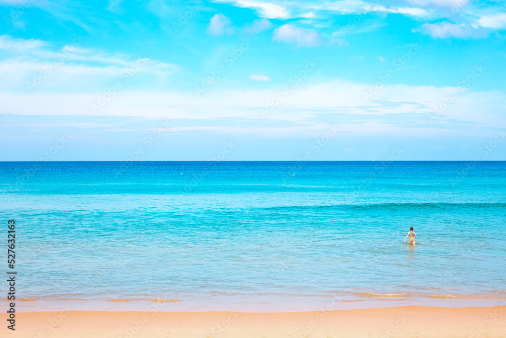 Blue sea with a strip of sandy beach and blue sky. In the background, a child enters the water. Seascape on a sunny day in the tropics