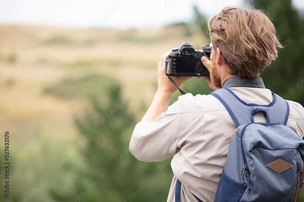 young man trekking among trees and taking pictures