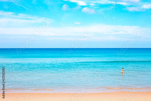 Blue sea with a strip of sandy beach and blue sky. In the background, a child enters the water. Seascape on a sunny day in the tropics © Natalia