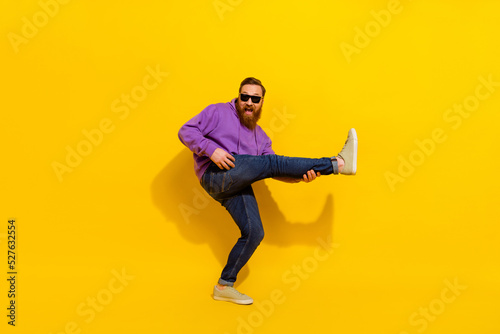 Full length photo of handsome positive guy dressed purple sweater eyewear dancing playing leg guitar isolated yellow color background
