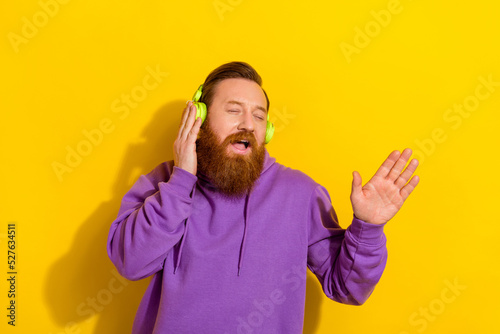 Photo of funny dreamy man wear violet sweatshirt hands earphones singing closed eyes isolated yellow color background © deagreez