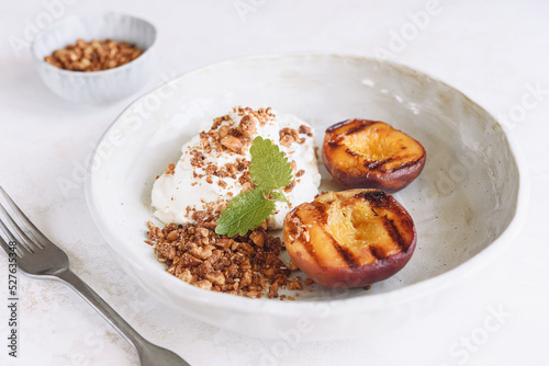 Summer dessert. Organic grilled peaches served with stracciatella cheese and caramelized nuts crumb on white background. Selective focus