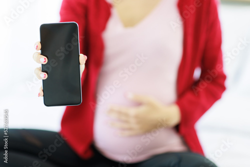 A pregnant woman's hand holds and shows a blank black screen of a smartphone