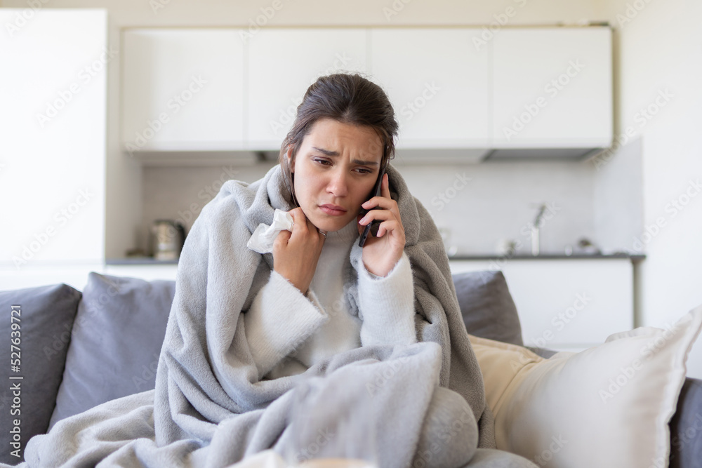 Ill upset woman calling doctor sitting on sofa with running nose, covered with blanket, freezing, got fever caught cold. Sick girl having influenza symptoms at home, flu concept. Ill upset woman calling doctor sitting on sofa with running nose, covered with blanket, freezing, got fever caught cold. Sick girl having influenza symptoms at home, flu concept.