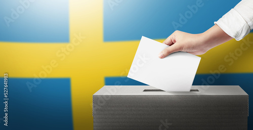 Close-up hand holding ballot paper into the voting box an Sweden flag background. Freedom democracy concept. Freedom vote concept. photo