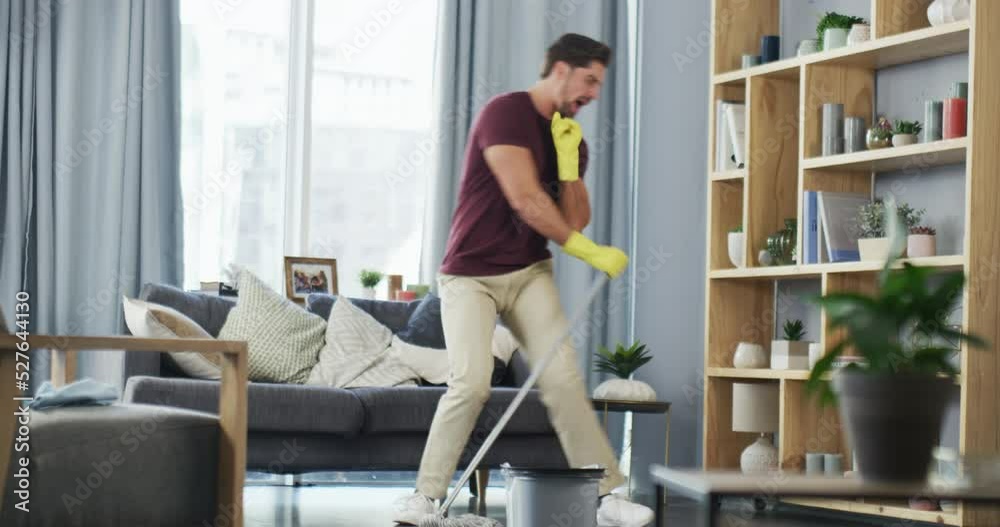 Cleaning, dancing and funny young man in house busy with spring cleaning in living room. Happy, crazy and singing male taking mopping dance break for fun while he does lounge tidy task.