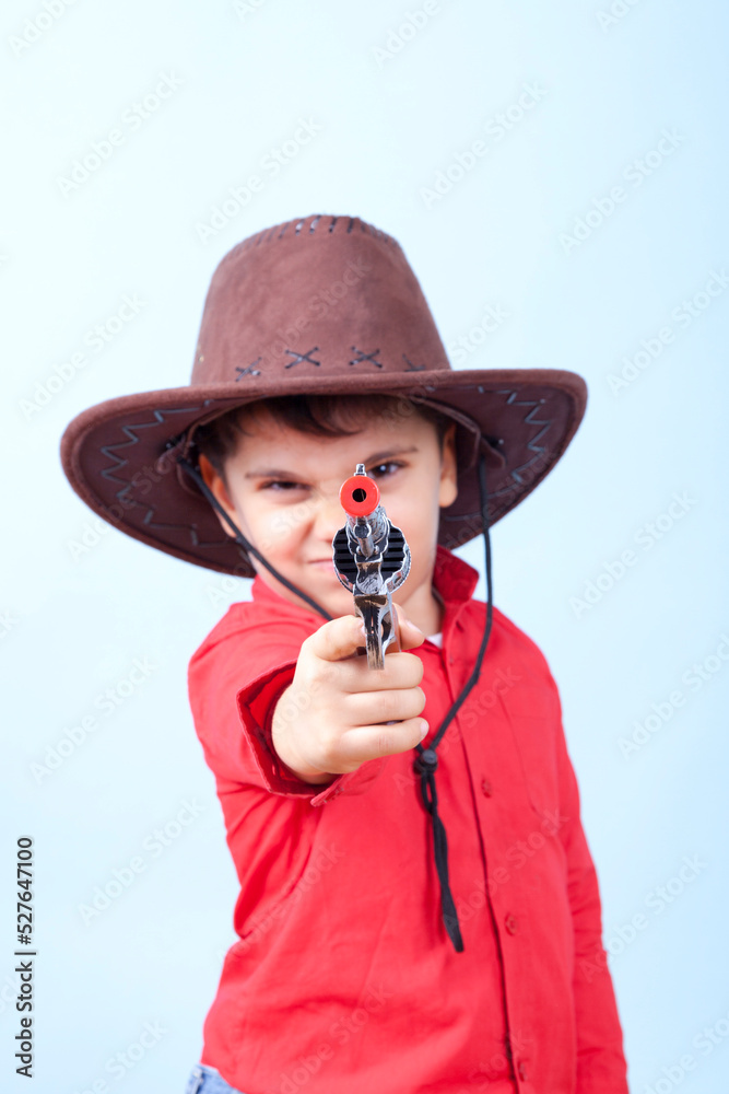 Naklejka premium Little Dangerous Cowboy is Pointing His Toy Gun Against Blue