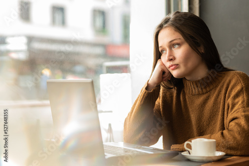 Self employed woman looking away thoughtfully during remote work in cafe
