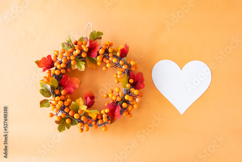 ハートと華やかな秋のオレンジ色の葉や実のリース（オレンジ色の背景）