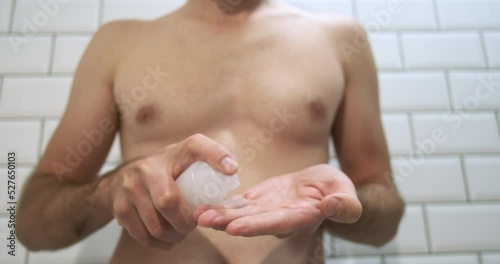 Unrecognizable man in the bathroom, sprays intimate gel lubricant on his fingers, drops fall down. Preparing for sex. Front view, close-up. photo