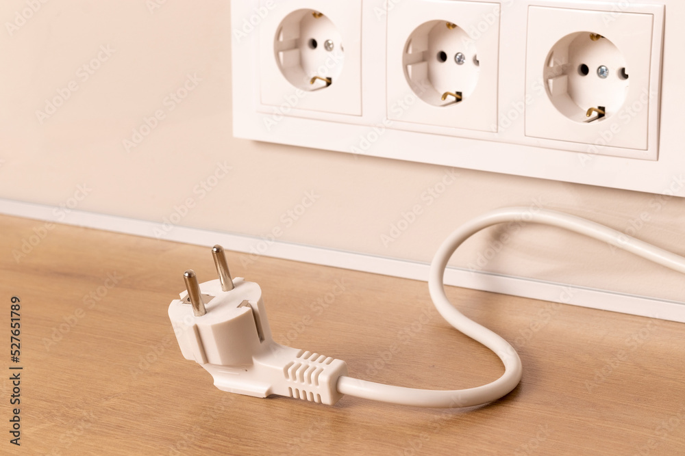 Power cord cable unplugged with group of white european electrical outlets on modern beige wall