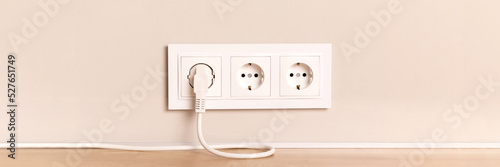 Group of white european electrical outlets with plug inserted into it on modern neutral beige wall with copy space banner. Wide panoramic header photo