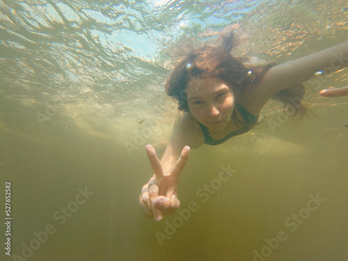 A young woman freediving, free diving, breath-hold swimming under water. Smiling swimmer who dives. Summer vacations, healthy lifestyle, amateur sport, leisure activity concepts