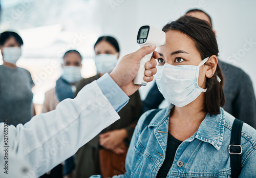 Covid screening with a female tourist in a mask having her temperature taken with an infrared thermometer while waiting to board in an airport. Travel restrictions during the corona virus pandemic