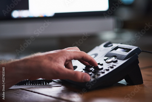 Closeup of a corporate business man making a telephone call to a colleague, partner or client. A company employee, male executive or industry professional using a desk phone to contact a department