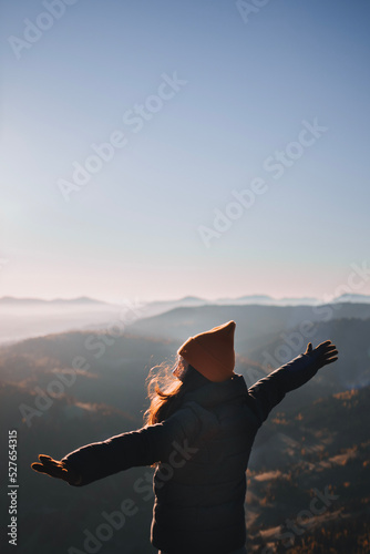 Happy woman from behind raises her hands up in front of the high mountains