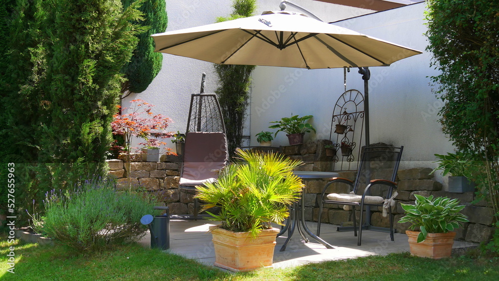 Gartenterrasse mit Sitzgruppe, Sonnenschirm und Hängeschaukel in einer Gartenecke mit Säulen-Faulbaum, Zypressen, Palme, Lavendel und Funkien