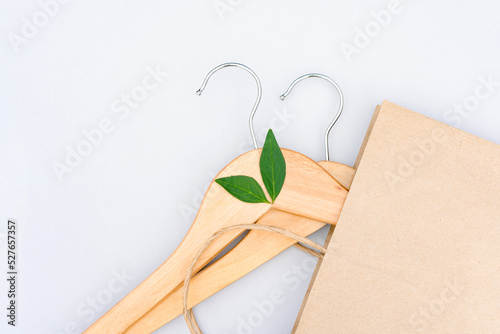 Green shopping concept. Wooden hangers, paper bag and green leaves over light gray background. Symbol of slow fashion. Reuse, recycling and upcycling clothes photo