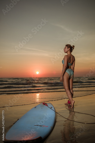 Young woman wearing  bikini standing beside the surf board for sup surfing on the beach at the sea on sunset of day,holliday summer vacation concept,shilouete photo,