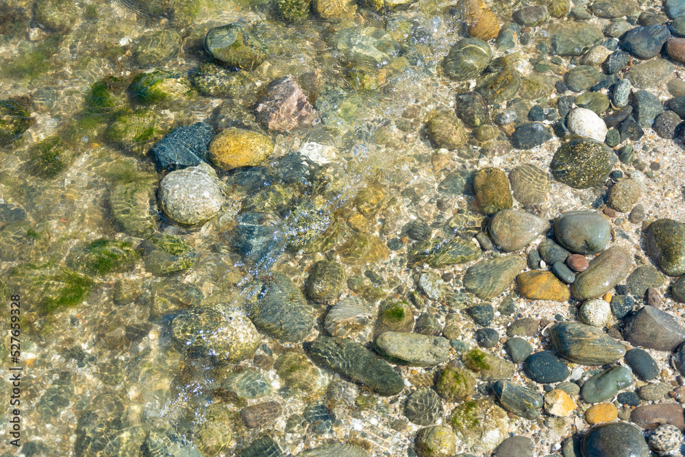 Sea pebbles in shallow water near the sea on a sunny day.