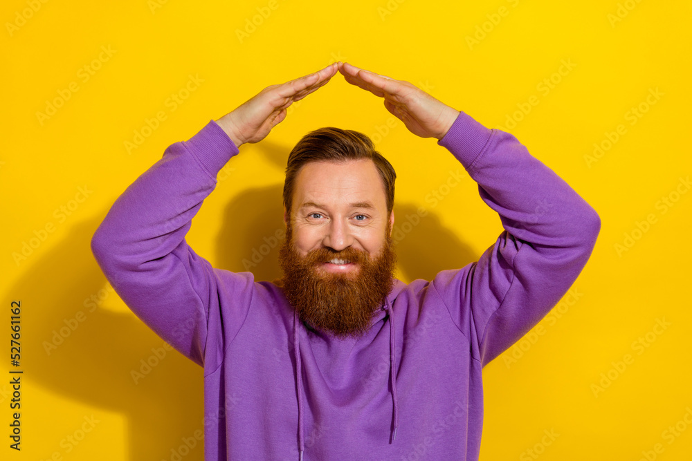 Photo of positive cute man wear violet sweatshirt showing arms roof space isolated yellow color background Photo of positive cute man wear violet sweatshirt showing arms roof space isolated yellow color background