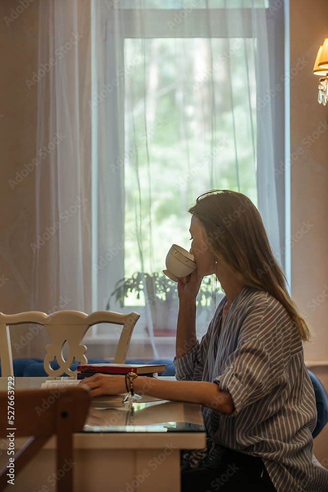 beautiful student girl with long hair drinks coffee in the dining room and reads special educational literature, prepares for classes, exam beautiful student girl with long hair drinks coffee in the dining room and reads special educational literature, prepares for classes, exam