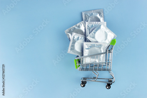 Many condoms in foil packaging in a shopping cart on a blue background. Safe sex and reproductive health concept.