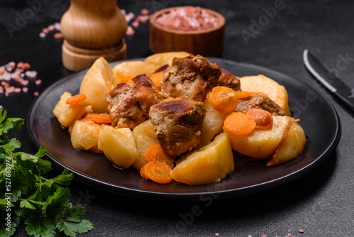 Beef meat and vegetables stew on a black plate with roasted potatoes