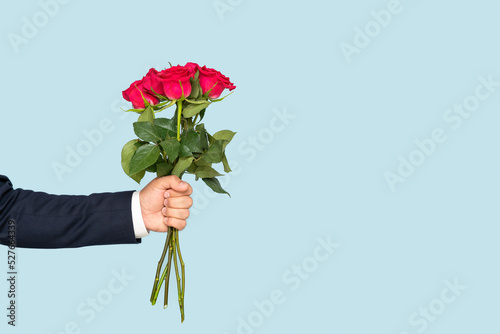 Fototapeta Naklejka Na Ścianę i Meble -  A man's hand holds out a bouquet of roses on a blue background