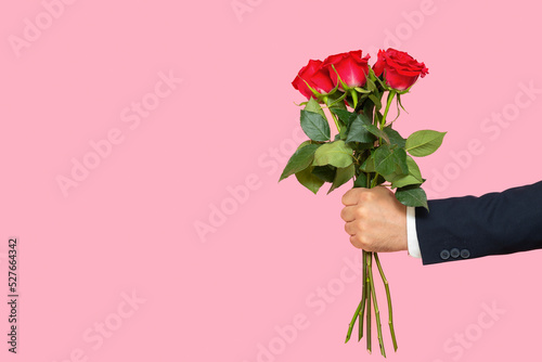Foto A man's hand with a bouquet of red roses on a pink background