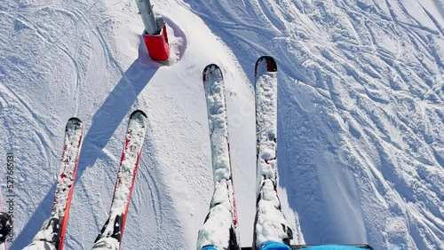 View from ski lift: legs and pairs of skis over skier below