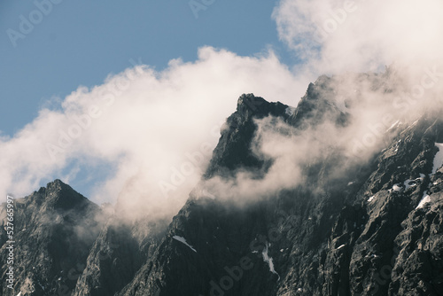 The cloud is stuck in the snowy rocky peak of the high mountain. Air element. Wind, clouds, bad weather, before storm, dangerous climbing theme. Concept of climate. landscape photo for wallpaper