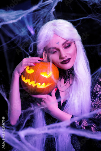 Sexy witch with hallowen makeup and long white hair holding pumpkin on black background