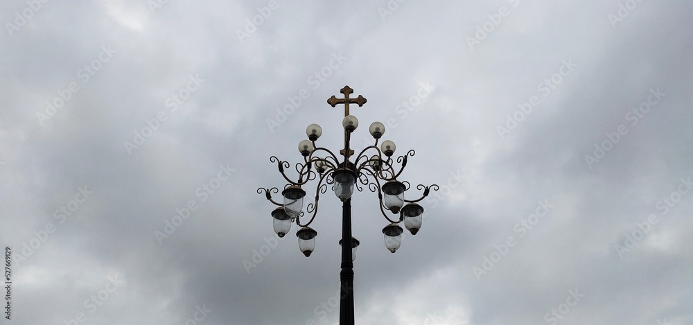 Old traditional antique and vintage christian religion symbol holy gold cross outdoor light bulb pole isolated on white sky clouds background with copy space. Graveyard, cemetery and funeral concept.