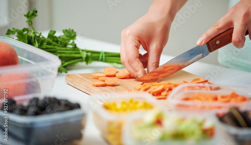 Fototapeta Naklejka Na Ścianę i Meble -  Close-up knife in female hands chopping fresh carrot on wooden board while preparing vegetables for freezing. Storage for winter storage in trays