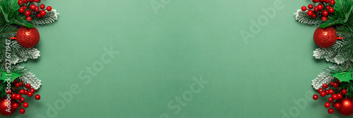 Bright Christmas border made with fir tree branches, berries and bright balls on green background with copy space for your design. Invitation card template. Long banner format.