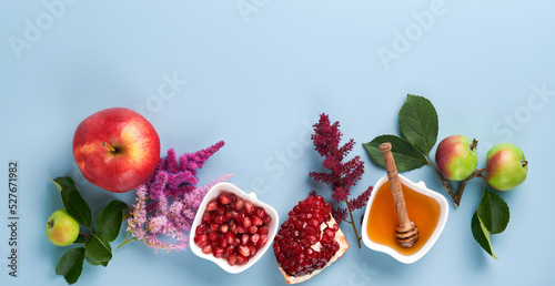 Rosh Hashanah. Honey jar, honeycomb, apple and pomegranate on simple blue background. Jewish New Year holiday greeting card. Rosh Hashanah holiday attributes. Banner.