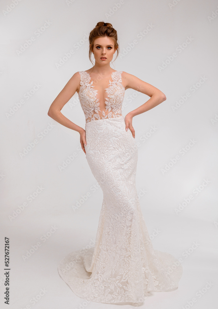 Beautiful bride lady posing in an elegant white wedding dress with lace in spacious studio room looking into camera having stylish wedding haircut. Bride woman model. Full length bride portrait. Beautiful bride lady posing in an elegant white wedding dress with lace in spacious studio room looking into camera having stylish wedding haircut. Bride woman model. Full length bride portrait.
