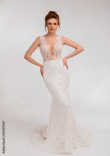 Beautiful bride lady posing in an elegant white wedding dress with lace in spacious studio room looking into camera having stylish wedding haircut. Bride woman model. Full length bride portrait.