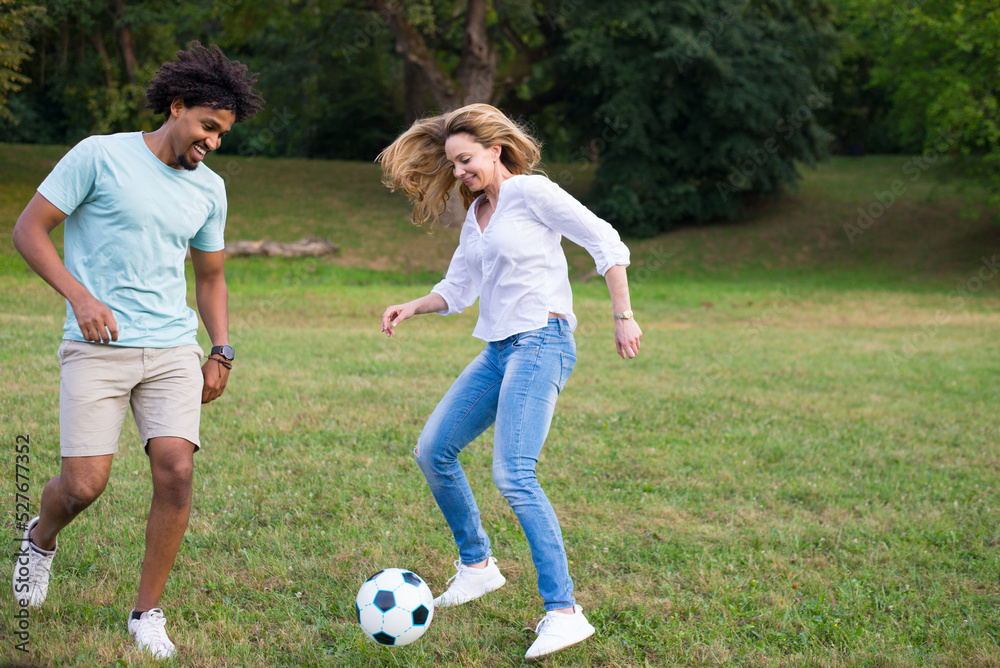 Young mixed race  couple playing football on the summer meadow