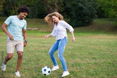 Young mixed race couple playing football on the summer meadow