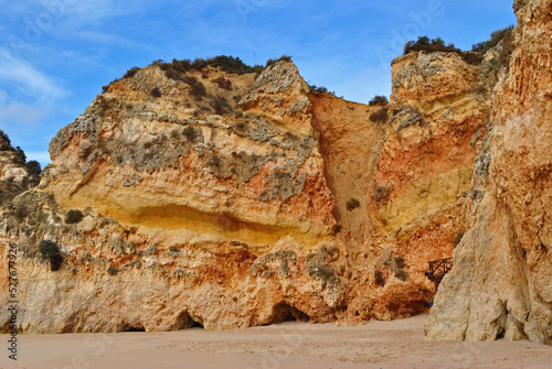 Sandy Beach with Eroded and Textured Stone Cliff Face and Blue Sky 