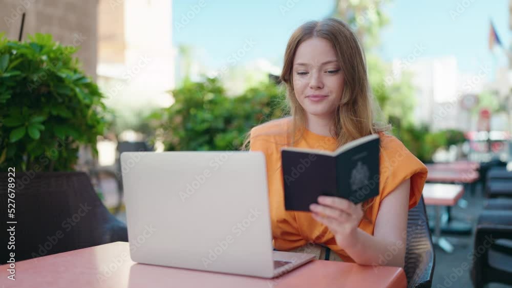 Young woman using laptop hiolding passport at coffee shop terrace Young woman using laptop hiolding passport at coffee shop terrace