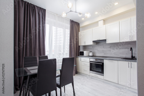 Clean kitchen in a small cozy contemporary studio apartment. Table and chairs in the foreground. Built in household appliance