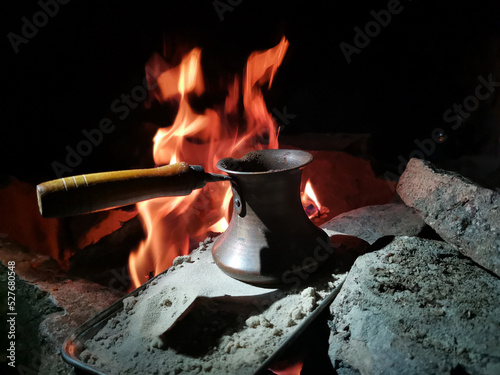 Coffee in cezve on the sand against the background of a night campfire photo