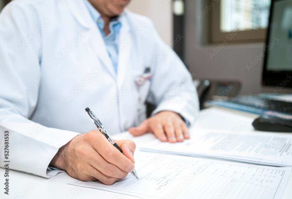 cardiologist looking at electrocardiograph ekg paper filling patient form. sitting and writing notes at the desk in clinic or hospital Office cardiologist looking at electrocardiograph ekg paper filling patient form. sitting and writing notes at the desk in clinic or hospital Office