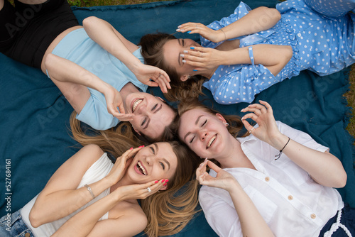 Top view of young laughing women raising hands to face, lying in circle on blue blanket with closed eyes, having fun.